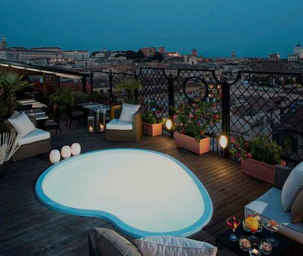 Kuva kattoterassista, jolla on pieni uima-allas, istumapaikkoja ja näkymä kaupunkiin hämärässä. (Tekoälyn luoma teksti)
