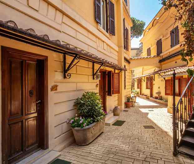 Aurinkoinen sisäpiha, jossa on hiekkakeltaisia rakennuksia, portaita ja kukkaistutuksia. (Tekoälyn luoma teksti)