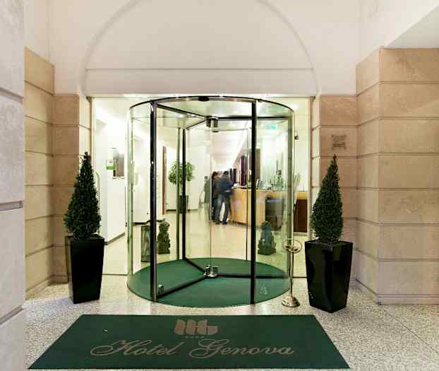 Hotel Genovan sisäänkäynti lasiovilla, vihreä matto ja kaksi koristeltua kasvia. (Tekoälyn luoma teksti)