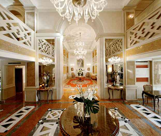 Tyylikäs hotellin aula, jossa on kattokruunuja, peilejä ja keskellä pöytä kukilla. (Tekoälyn luoma teksti)