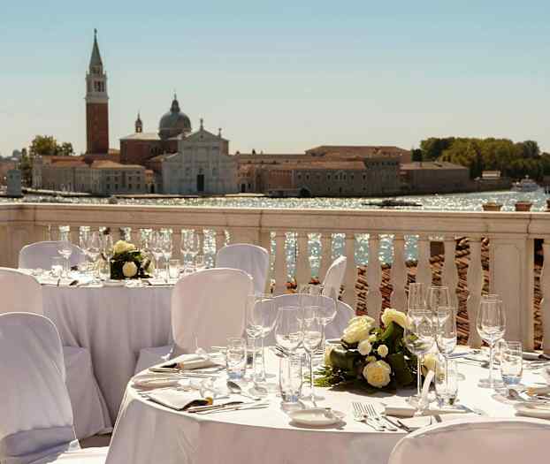 Ulkona sijaitseva illallinen terassilla, jolta avautuu näkymä historialliseen rakennukseen veden äärellä. (Tekoälyn luoma teksti)