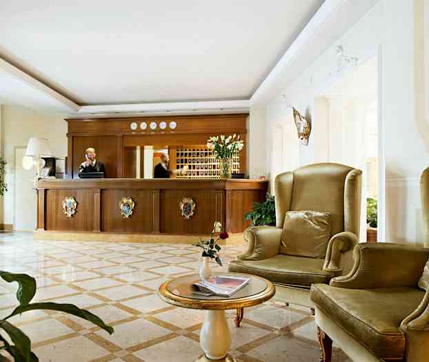 Hotellin vastaanottoalue, jossa on puinen vastaanottotiski ja istumapaikkoja vihreillä nojatuoleilla. (Tekoälyn luoma teksti)