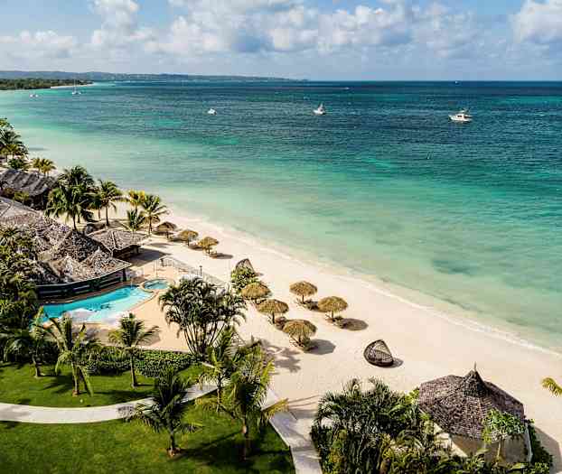 Ranta, jossa on aurinkovarjoja, ja lomakeskus uima-altaalla. (Tekoälyn luoma teksti)