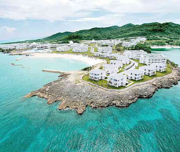 Ilmakuva rannikkomaastosta, jossa on valkoisia rakennuksia vehreyden ja turkoosinsinisen veden ympäröimänä. (Tekoälyn luoma teksti)