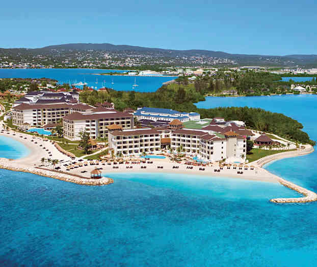 Lomakeskus merenrannalla, jossa hiekkarantoja ja uima-altaita, vehreyden ja sinisen veden ympäröimänä. (Tekoälyn luoma teksti)