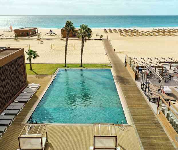 Ulkouima-allas aurinkotuoleineen, nurmikko, ranta aurinkovarjoineen ja meri taustalla. (Tekoälyn luoma teksti)