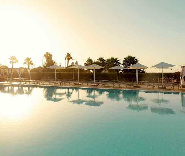 Uima-allasalue aurinkotuoleilla ja aurinkovarjoilla auringonlaskun aikaan. (Tekoälyn luoma teksti)