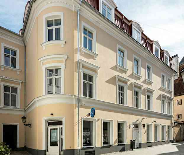 Beige rakennus, jossa on valkoisia yksityiskohtia ja punaiset katot, kaupunginosassa. (Tekoälyn luoma teksti)