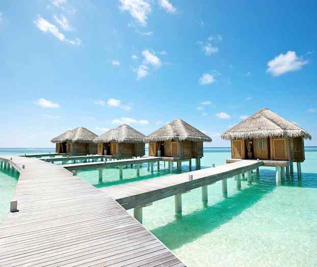 Rivistö vesillä olevia bungaloweja turkoosinsinisessä vedessä sinisen taivaan alla. (Tekoälyn luoma teksti)