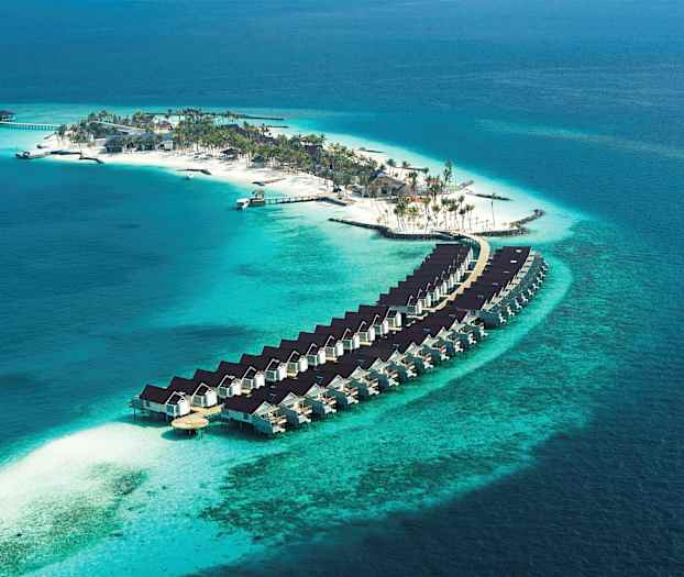 Ilmakuva saaresta, jossa ranta, palmuja ja veteen rakennettuja asuntoja. (Tekoälyn luoma teksti)