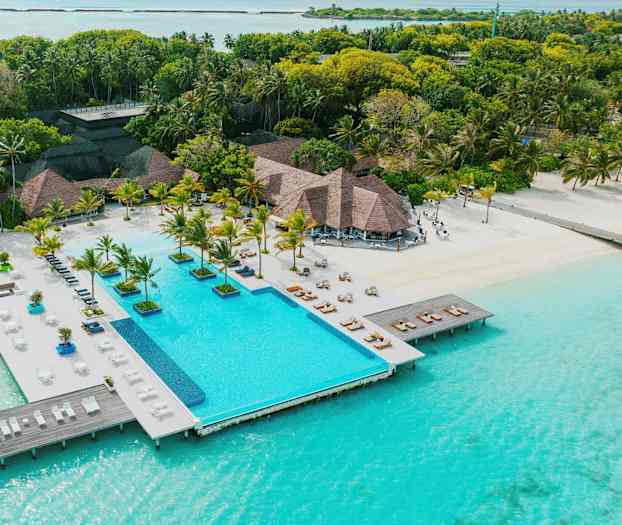 Lomakeskus, jossa uima-allas sijaitsee aivan turkoosinsinisen veden äärellä ja jota ympäröivät palmut ja vehreys. (Tekoälyn luoma teksti)