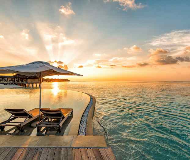 Kaksi aurinkotuolia ja varjo poolin äärellä ja meri auringonlaskussa. (Tekoälyn luoma teksti)