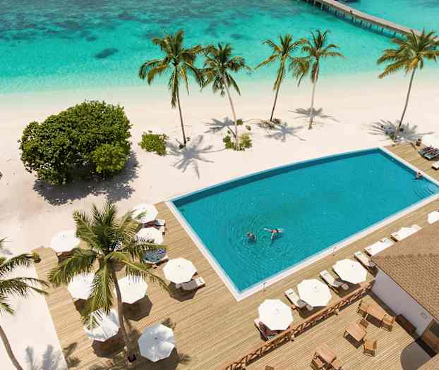 Näkymä allasalueelle, jossa aurinkotuoleja trooppisella rannalla, palmuja ja kristallinkirkasta vettä ympäröivät. (Tekoälyn luoma teksti)