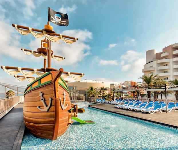 Kuva uima-allasalueesta, jossa on leikkimerirosvolaiva ja aurinkotuoleja taustalla. (Tekoälyn luoma teksti)