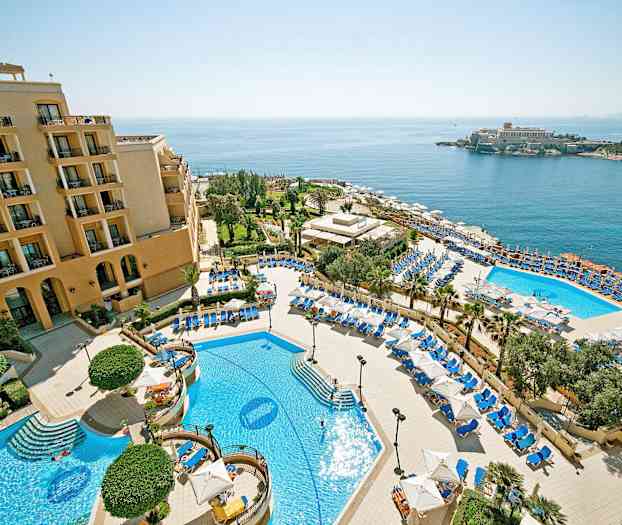 Hotellialue, jossa on uima-altaita, aurinkotuoleja ja aurinkovarjoja sekä merinäköala. (Tekoälyn luoma teksti)