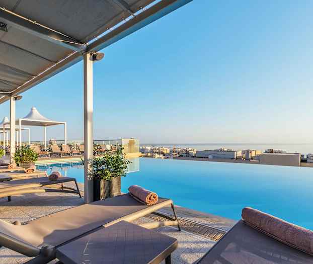 Aurinkotuoleja infinity-altaan äärellä näköalalla kaupunkiin ja merelle. (Tekoälyn luoma teksti)