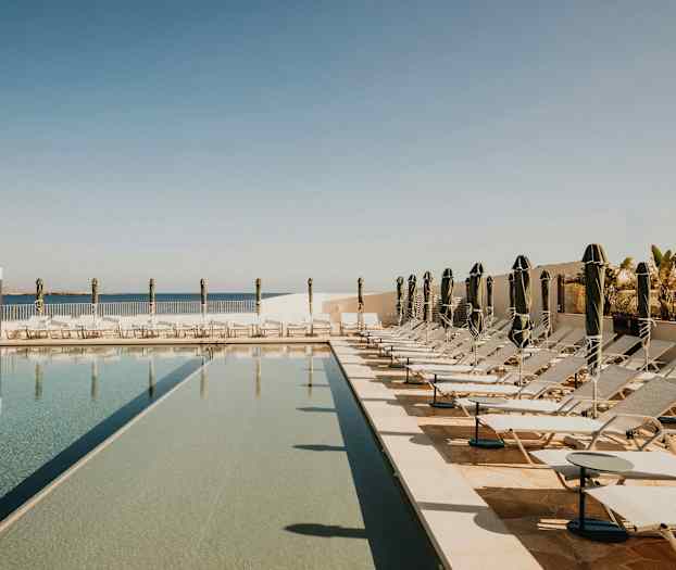 Kuva uima-altaasta aurinkotuoleineen ja aurinkovarjoineen aurinkoisella ulkoalueella. (Tekoälyn luoma teksti)