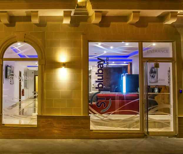 Rakennuksen sisäänkäynti lasi-ikkunoin ja -ovineen, valaistuna illalla. (Tekoälyn luoma teksti)