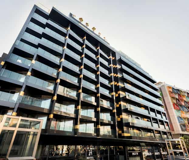 Nykyaikainen rakennus, jossa on lasiseinät ja parvekkeet. Vieressä toinen rakennus värillisillä paneeleilla. (Tekoälyn luoma teksti)