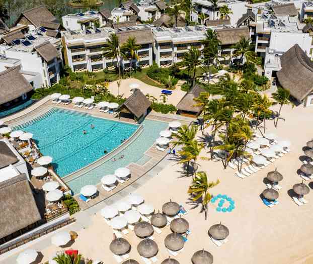 Lentoilmasta otettu näkymä hotellialueesta, jossa on uima-allas, viheralueita ja aurinkovarjoja hiekkarannalla. (Tekoälyn luoma teksti)