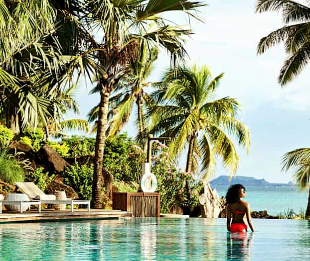 Henkilö istuu uima-altaassa, josta on näkymä trooppisille palmuihin ja merimaisemaan. (Tekoälyn luoma teksti)