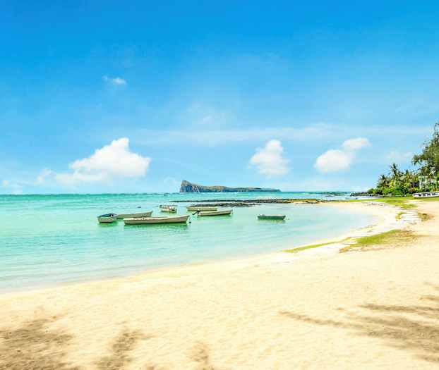 Hiekkaranta, jolla pieniä veneitä kirkkaassa vedessä ja kasvillisuutta reunalla. (Tekoälyn luoma teksti)