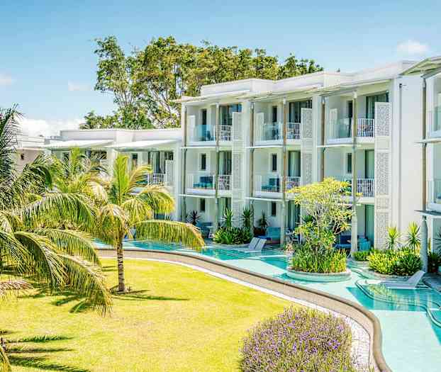 Moderni lomahotelli, jossa on valkoiset rakennukset ja parvekkeet vehreän trooppisten kasvien puutarhan ympäröimänä. (Tekoälyn luoma teksti)