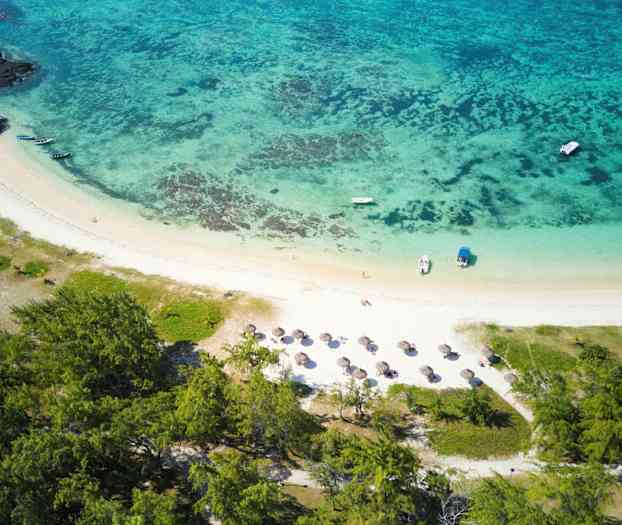 Ilmakuva trooppisesta rannasta, jossa on aurinkovarjoja, veneitä ja ympäröivää vehreyttä. (Tekoälyn luoma teksti)