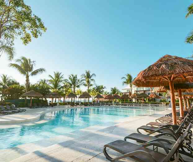 Uima-allas aurinkotuolien ja palmujen ympäröimänä kirkkaan taivaan alla. (Tekoälyn luoma teksti)