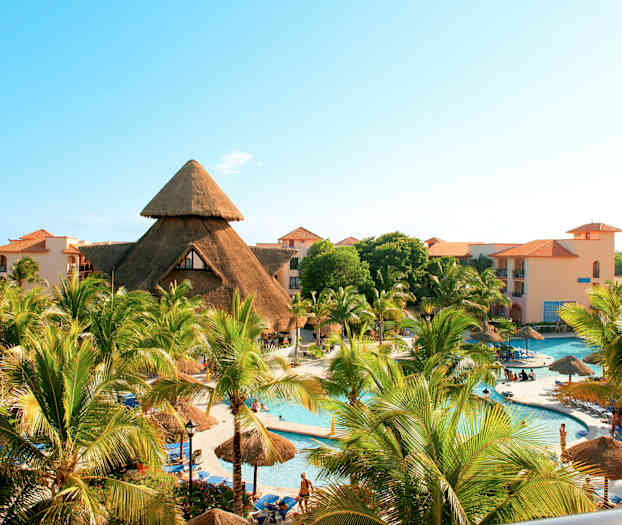 Lomakeskus, jossa uima-allas, palmuja ja rakennuksia, joiden katot ovat pyöreitä ja olkikattoisia. (Tekoälyn luoma teksti)