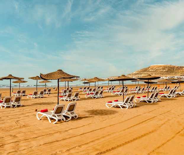 Aurinkotuoleja ja varjoja hiekkarannalla. (Tekoälyn luoma teksti)