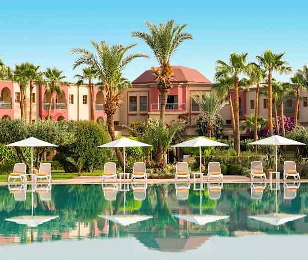 Uima-allas rakennuksen edessä, jota ympäröivät palmut ja aurinkovarjot. (Tekoälyn luoma teksti)