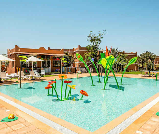 Ulkouima-allas, jonka vesileikkivälineet on muotoiltu kukkamaisiksi hahmoiksi vihreänä ja oranssina, ympärillä aurinkotuoleja ja aurinkovarjoja. (Tekoälyn luoma teksti)