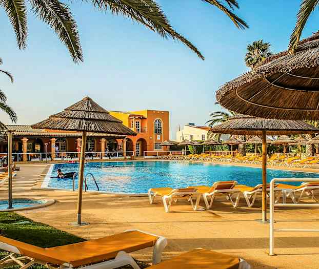 Ulkouima-allas, jota ympäröivät aurinkotuolit ja olkikattoiset varjot, taustalla rakennus. (Tekoälyn luoma teksti)