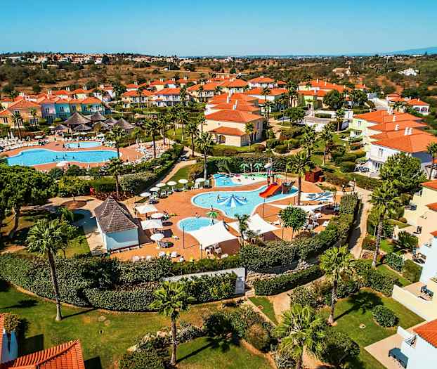 Ilmakuva lomakeskuksesta, jossa on uima-altaita ja värikkäitä taloja. (Tekoälyn luoma teksti)