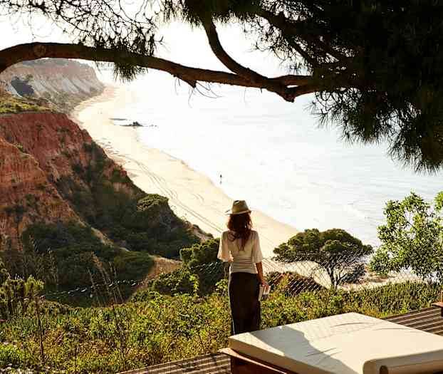 Nainen seisoo reunalla katsellen hiekkarantaa ja kallionmuodostelmia. (Tekoälyn luoma teksti)