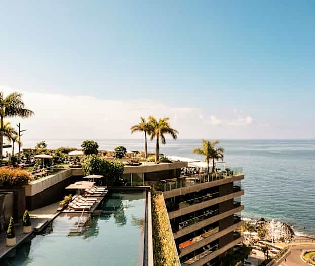 Näkymä hotellialueelle meren rannalla, jossa on uima-altaita ja palmuja. (Tekoälyn luoma teksti)