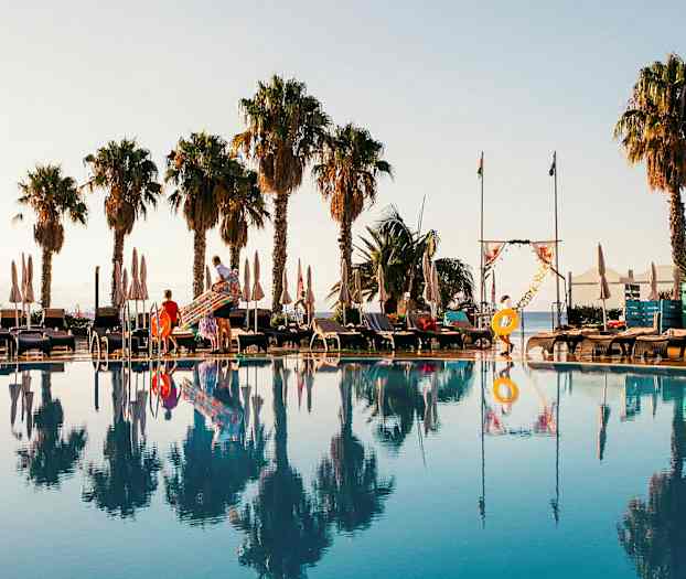 Uima-allasalue aurinkotuoleilla, aurinkovarjoilla ja palmujen taustalla. (Tekoälyn luoma teksti)