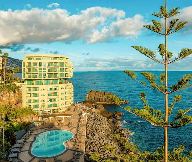 Hotelli rannalla, jossa on uima-allas ja jota ympäröi meri ja puita. (Tekoälyn luoma teksti)