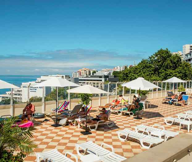 Aurinkoterassi, jossa on aurinkotuoleja ja varjoja, näkymä merelle. (Tekoälyn luoma teksti)