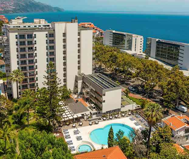 Hotellirakennus uima-altaalla ja ympäröivällä vihreydellä, meri taustalla. (Tekoälyn luoma teksti)