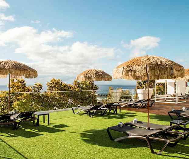 Aurinkotuoleja pyyhkeillä ja varjoja nurmikolla, josta on näkymä merelle. (Tekoälyn luoma teksti)