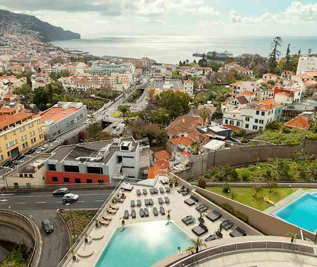 Näkymä kaupungista rakennuksineen, teineen, kaksi uima-allasta ja taustalla oleva meri. (Tekoälyn luoma teksti)