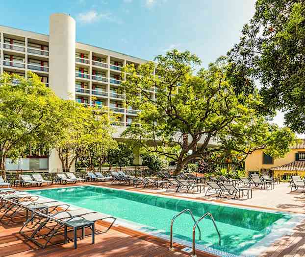 Ulkouima-allas aurinkotuoleilla, ympäröity puilla ja rakennuksilla. (Tekoälyn luoma teksti)