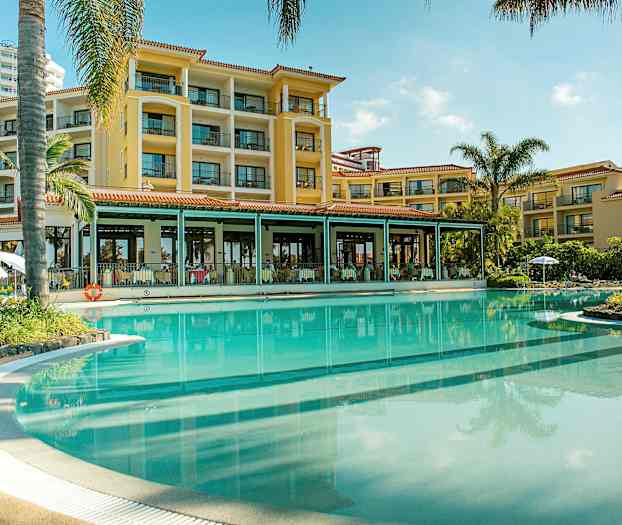 Hotellin julkisivu suuren uima-altaan äärellä, jota ympäröivät palmut. (Tekoälyn luoma teksti)