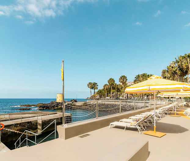 Aurinkotuoleja ja aurinkovarjoja rannikon äärellä merinäköalalla. (Tekoälyn luoma teksti)