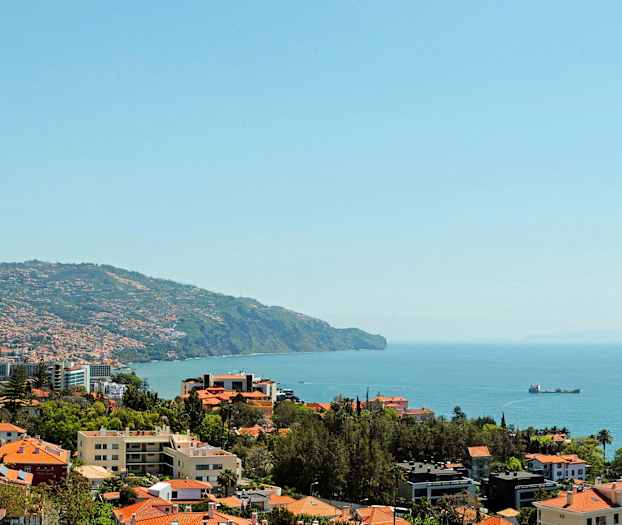 Näkymä rannikkokaupunkiin, jossa punakattoisia taloja ja taustalla näkyy meri. (Tekoälyn luoma teksti)