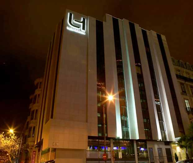 Moderni hotelli, jonka ulkokuori on kuvattu yöllä. Rakennuksen julkisivu on valaistu. (Tekoälyn luoma teksti)