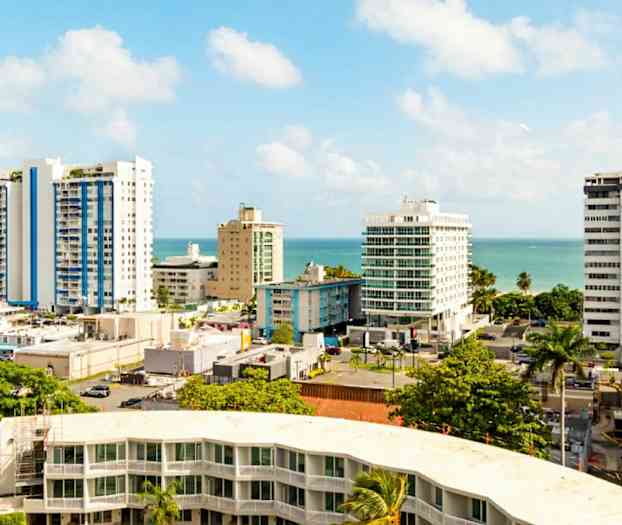 Kaupunkinäkymä korkeista rakennuksista ja palmuista lähellä merta kirkkaan sinisen taivaan alla. (Tekoälyn luoma teksti)