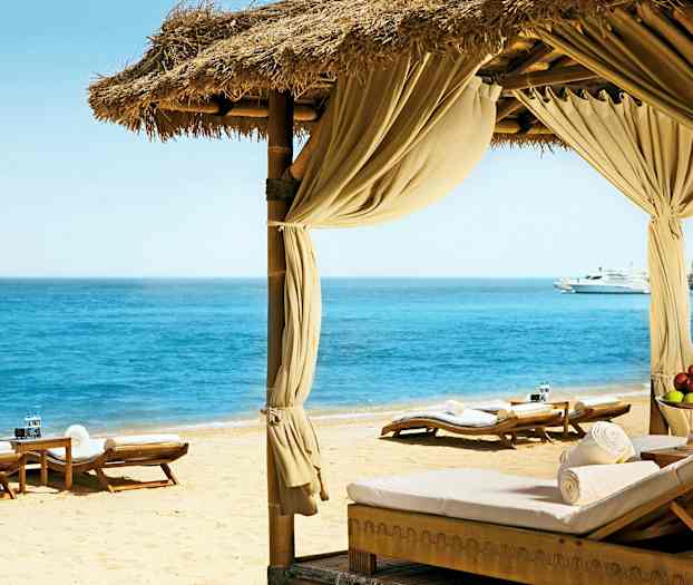 Ranta, jossa aurinkotuoleja ja paviljonki avautuu kohti kirkasta merta. (Tekoälyn luoma teksti)